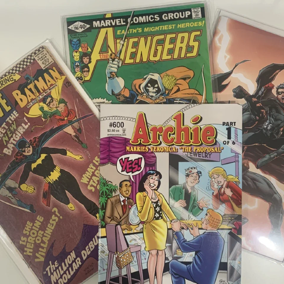 A stack of raw comic books — Avengers, Batman, Archie — in protective capsules